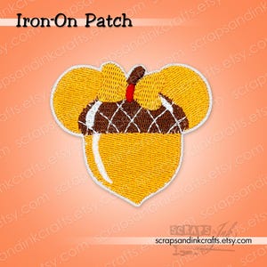 May include: Embroidered iron-on patch in the shape of an acorn. The patch features a yellow body with a brown and white top, and a red accent. The text "Iron-On Patch" is at the top.