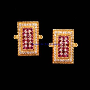 May include: A pair of rectangular gold rings featuring a central cluster of round pink gemstones surrounded by a border of small clear white stones. The gold bands are polished and the settings have a textured edge. The text jewels-treasure is visible.