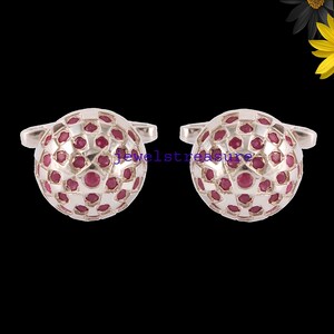 Peut inclure: Une paire de boutons de manchette ronds avec un motif en treillis métallique argenté incrusté de petites pierres précieuses rouges circulaires. Le texte "jeweltreasure" est visible en lettres bleues au centre des deux faces sphériques.