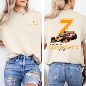 May include: Beige t-shirt featuring the text "Lundgaard" and a logo on the front. The back of the shirt displays a large orange number 7, a race car graphic, and the name "Christian Lundgaard".