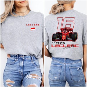 May include: Gray t-shirt with a red race car graphic on the back. The car has the number 16 and the name "Charles Leclerc" printed on it. The front of the shirt has the name "Leclerc" and a small flag printed on it.