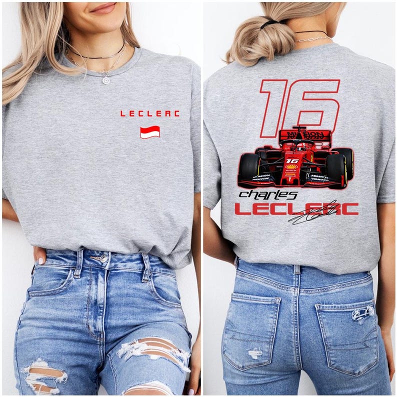 May include: Gray t-shirt with a red race car graphic on the back. The car has the number 16 and the name "Charles Leclerc" printed on it. The front of the shirt has the name "Leclerc" and a small flag printed on it.