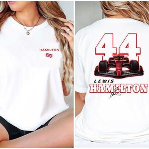 May include: White t-shirt with a red number 44 and a red race car on the back. The text "Lewis Hamilton" is printed below the car. The front of the shirt has the text "Hamilton" and a small British flag.
