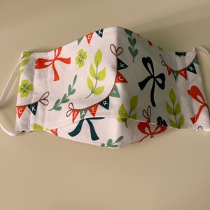 May include: White face mask with a pattern of red and green bows, green leaves, and flags with the letters "CK" and "PATRI" printed on them.