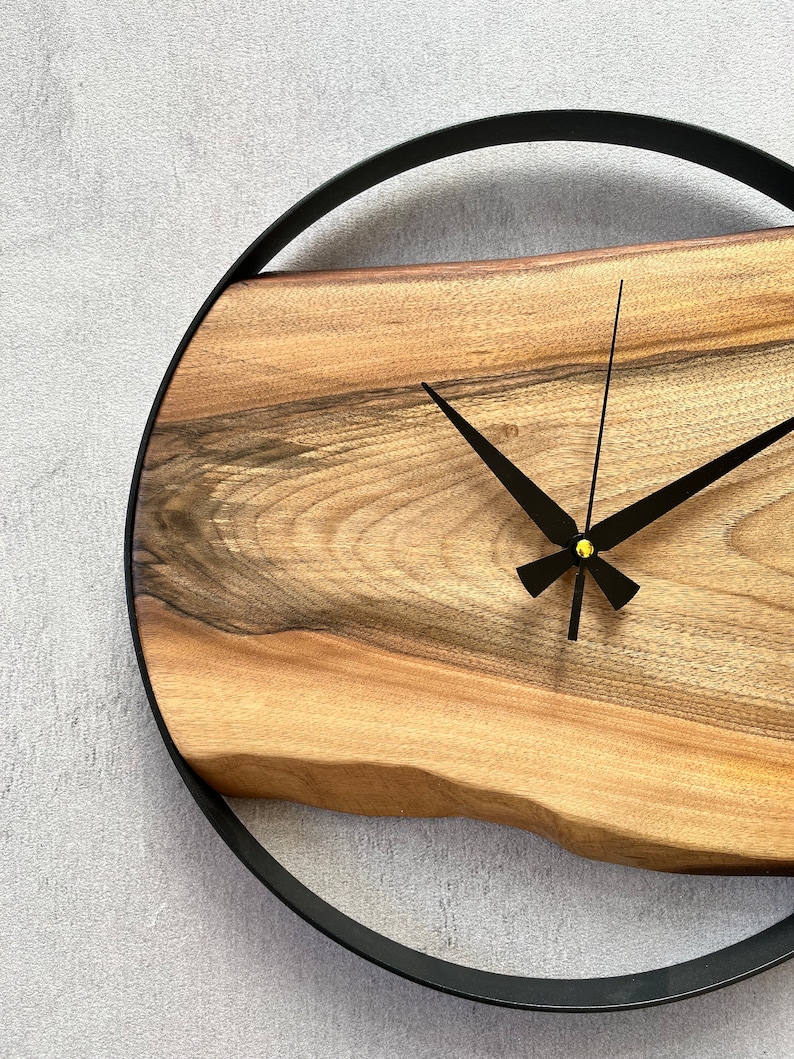 May include: A wooden wall clock with a black metal frame and black hands. The clock face is made of a natural wood slice with a unique grain pattern.
