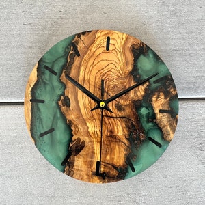 May include: A round wooden clock with a green and brown resin face. The clock has black hands and a gold center.