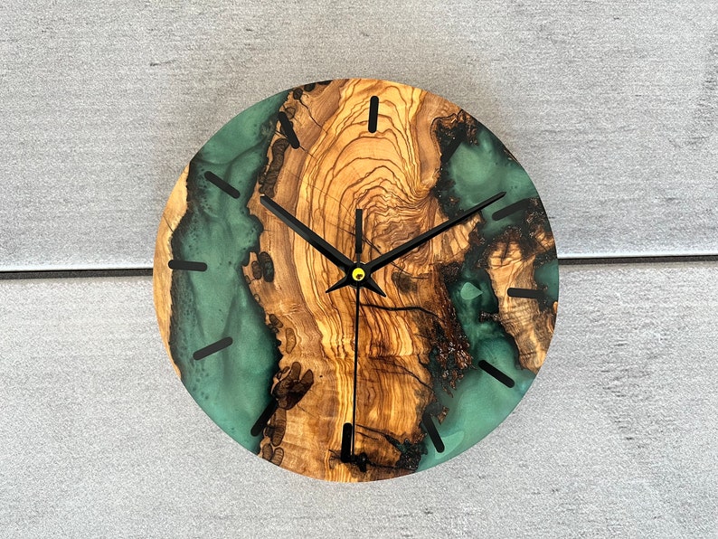May include: A round wooden clock with a green and brown resin face. The clock has black hands and a gold center.