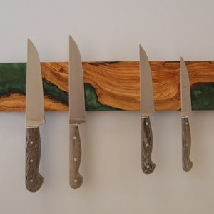 Może przedstawiać: Magnetyczny uchwyt na noże wykonany z drewna z zielonymi akcentami z żywicy epoksydowej. Pięć srebrnych noży jest przymocowanych do uchwytu.