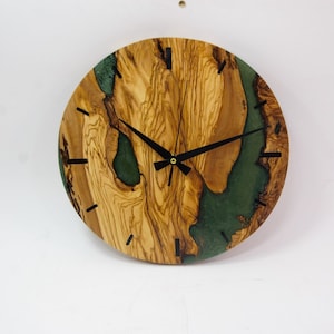 May include: A round wooden clock with a green resin inlay. The clock face has black hands and black Roman numeral markings.
