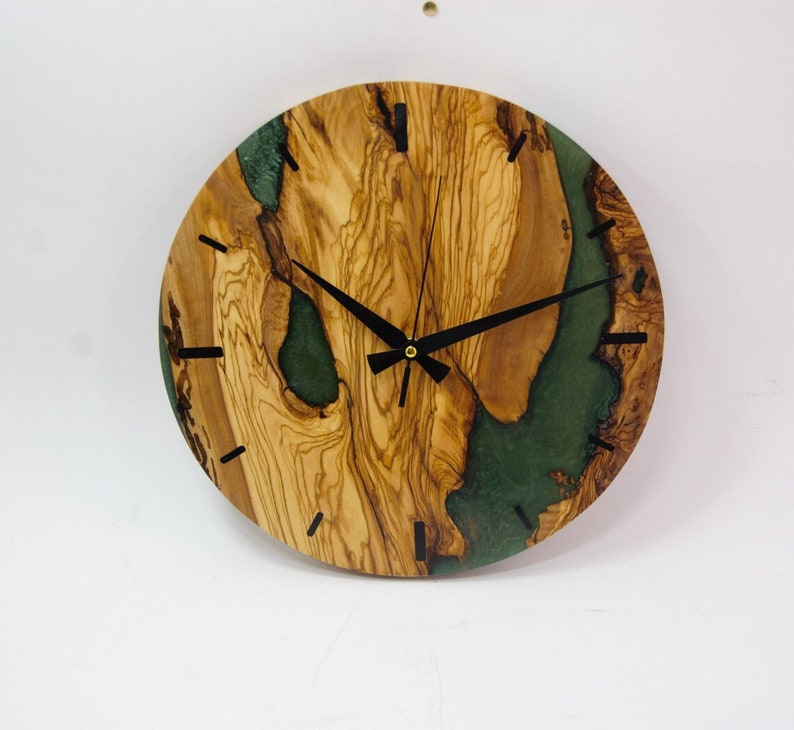 May include: A round wooden clock with a green resin inlay. The clock face has black hands and black Roman numeral markings.