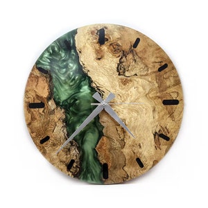 May include: A round wooden clock with a green resin inlay. The clock face has black Roman numeral hour markers and silver hands.
