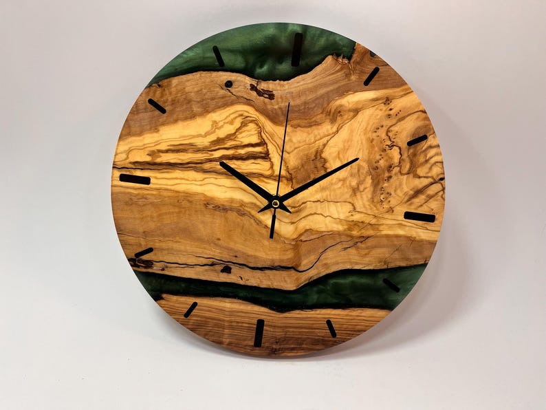 May include: A round wooden wall clock with a green epoxy resin inlay. The clock face has black hour and minute hands and black Roman numeral markings.
