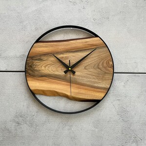 May include: A round wooden clock with black hands and a black metal frame. The wood has a natural grain pattern.