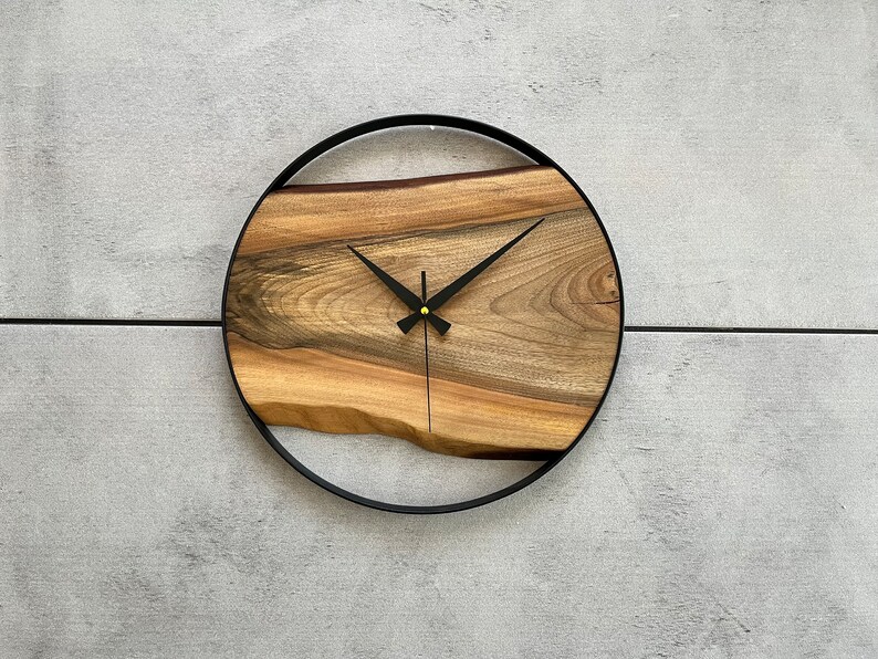 May include: A round wooden clock with black hands and a black metal frame. The wood has a natural grain pattern.