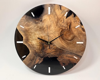 May include: A round wooden wall clock with black epoxy resin and white hour markers. The clock face is made of a natural wood slice with a unique grain pattern.
