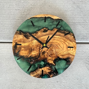 May include: A round wooden clock with a green and brown epoxy resin face. The clock has black hands and a gold center.