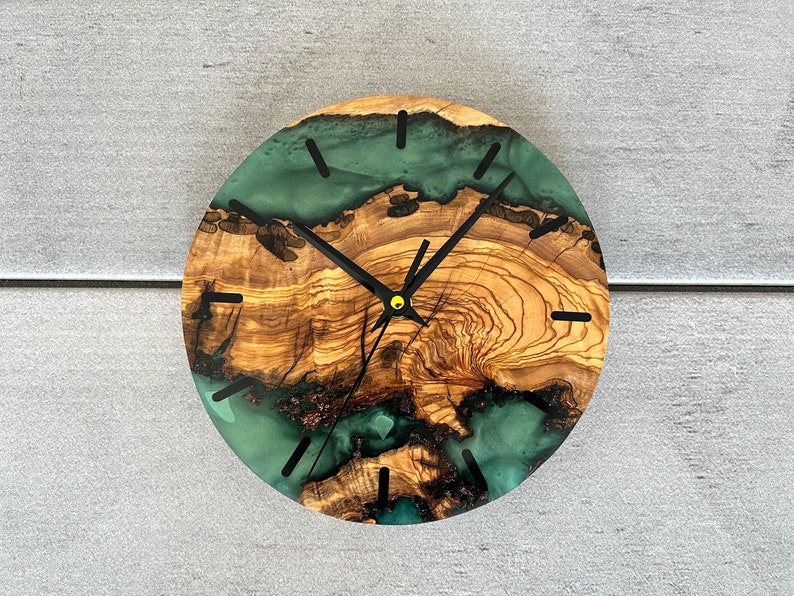 May include: A round wooden clock with a green and brown epoxy resin face. The clock has black hands and a gold center.