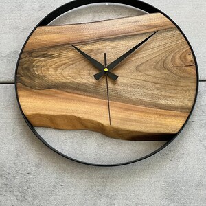 May include: A round wooden clock with black hands and a black metal frame. The wood has a natural grain pattern.