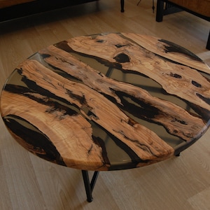 Op de afbeelding: Ronde houten salontafel met een zwarte epoxyhars inlay. De tafel heeft een natuurlijke houtkleur en een unieke, organische vorm.