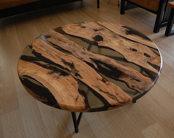 Op de afbeelding: Ronde houten salontafel met een zwarte epoxyhars inlay. De tafel heeft een natuurlijke houtkleur en een unieke, organische vorm.