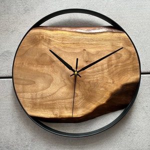 May include: A round wooden clock with black hands and a black metal frame. The wood has a natural, rustic look.