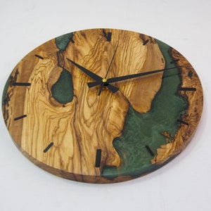 May include: A round wooden wall clock with a green epoxy resin inlay. The clock has black hands and black Roman numeral markings.