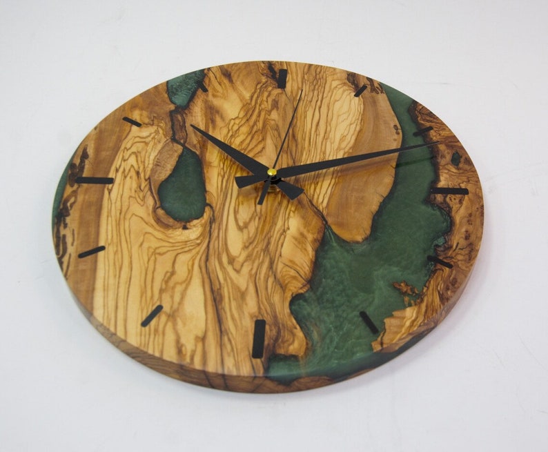 May include: A round wooden wall clock with a green epoxy resin inlay. The clock has black hands and black Roman numeral markings.