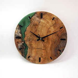 May include: A round wooden clock with a green epoxy resin inlay. The clock face has black hands and black Roman numeral markings.