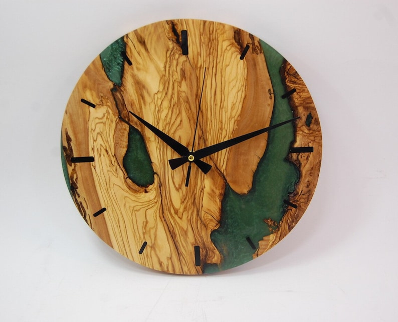 May include: A round wooden clock with a green epoxy resin inlay. The clock face has black hands and black Roman numeral markings.