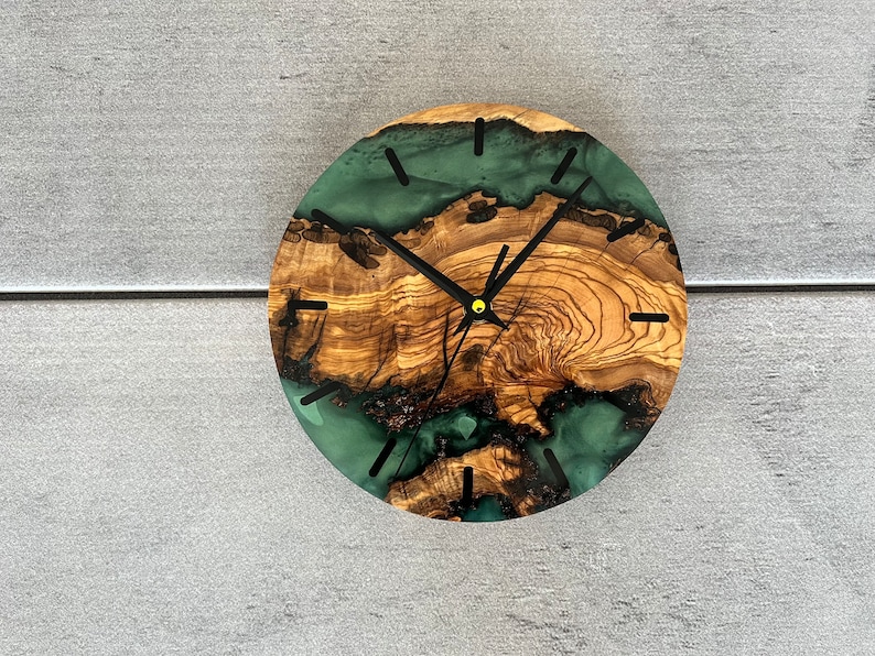 May include: A round wooden clock with a green epoxy resin inlay. The clock face has black hands and black Roman numeral markings.