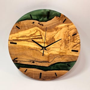 May include: A round wooden wall clock with a green epoxy resin inlay. The clock face has black hands and black Roman numeral markings.