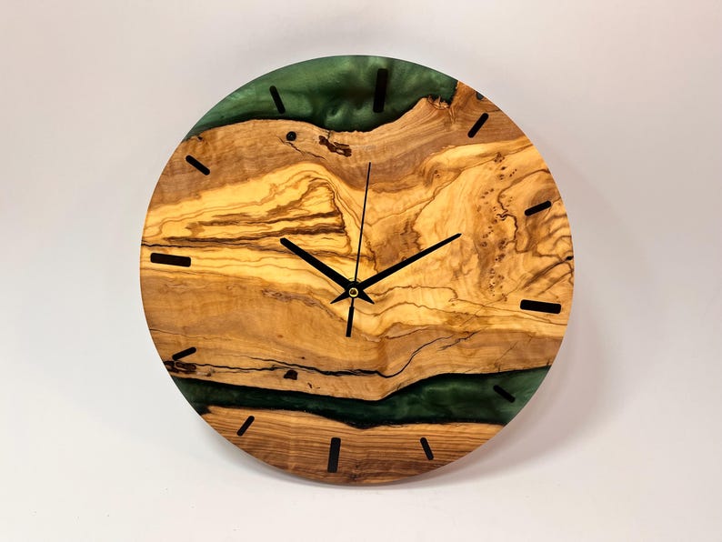 May include: A round wooden wall clock with a green epoxy resin inlay. The clock face has black hands and black Roman numeral markings.
