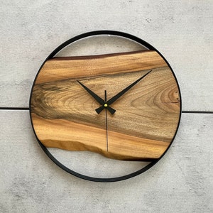 May include: A round wooden clock with black hands and a black metal frame. The wood has a natural grain pattern.