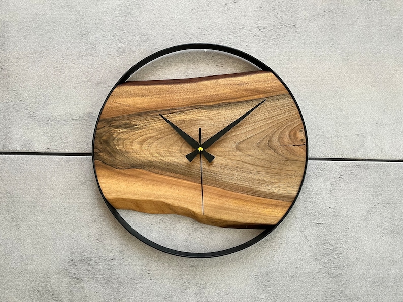 May include: A round wooden clock with black hands and a black metal frame. The wood has a natural grain pattern.