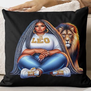 May include: Black cushion featuring a digital illustration of a person with long braided hair, wearing a white t-shirt with "LEO" text, blue jeans, and white trainers. A lion is behind the person. The cushion is a decorative item.