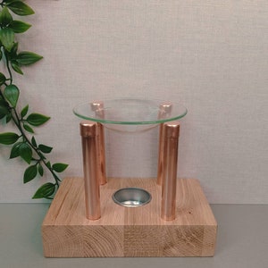 May include: Aromatherapy oil diffuser with a clear glass bowl supported by copper-colored metal legs on a wooden base. The base has a recessed area for a tea light. Decorative home decor.