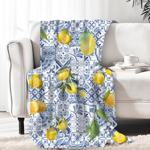 Puede incluir: Una manta de tiro azul y blanca con un patrón de limón. La manta presenta un patrón repetitivo de limones, hojas y azulejos azules y blancos.