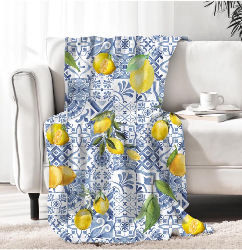 K&ouml;nnte beinhalten: Eine blaue und wei&szlig;e Wurfdecke mit einem Zitronenmuster. Die Decke hat ein sich wiederholendes Muster aus Zitronen, Bl&auml;ttern und blauen und wei&szlig;en Fliesen.
