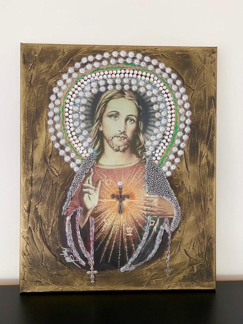May include: A painting of Jesus Christ with a beaded halo and a cross on his chest. The painting is on a canvas with a gold background.