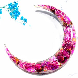 May include: A crescent moon-shaped resin tray with pink and purple dried flowers and glitter embedded inside.