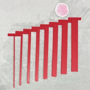 Könnte beinhalten: Ein Satz roter Kuchenmesswerkzeuge, jeweils mit Zollmaßen von 0,3 cm bis 2,5 cm beschriftet. Die Werkzeuge sind in absteigender Reihenfolge angeordnet, mit einem runden Aufkleber im Hintergrund mit der Aufschrift "MadebyCarey".