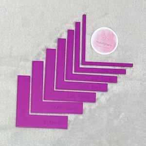Può includere: Un set di guide angolari a forma di L di colore magenta brillante, con misure da 3 mm a 2,5 cm, chiaramente indicate. È visibile anche un adesivo rotondo con la scritta "MadeByCarey".