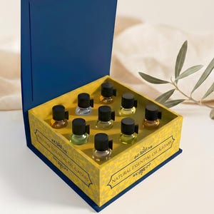 May include: A blue box with a yellow interior, holding small glass bottles with black caps. The box is open, displaying the bottles in rows. The box is labelled "Natural Essential Oil Kit".