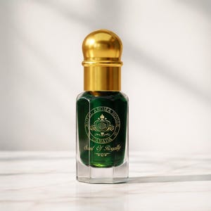 May include: A small, emerald green perfume bottle with a gold cap. The bottle has a clear, octagonal base and a gold label with the text "Royal Aroma House Canada" and "Scent Of Royalty". The background is a soft white.