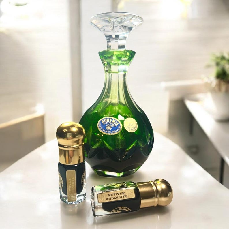May include: A green glass perfume bottle with a clear crystal stopper, flanked by two smaller bottles with gold caps. The large bottle has a label that reads "Bohemia". The smaller bottles are labeled "Vetiver Absolute".