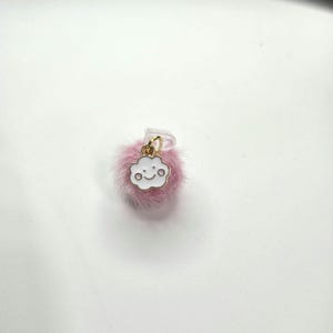 Peut inclure: Un petit accessoire rose et duveteux avec un fermoir doré. Un charm en forme de nuage blanc avec un visage souriant est suspendu au fermoir. L'accessoire est probablement un objet décoratif, peut-être pour un téléphone ou un sac.