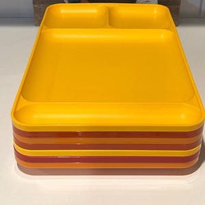 Könnte beinhalten: Ein Stapel gelber, geteilter Teller mit rotem und orangefarbenem Rand. Ein Holzschild im Hintergrund zeigt das Wort "hello" in weißer Schrift, umgeben von einem Blumengirlande mit Filzblumen.