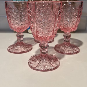 Könnte beinhalten: Set aus drei rosa Glaskelchen mit geschliffenem Glasdesign. Die Kelche haben einen runden Boden und einen hohen Stiel.