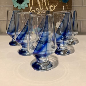 May include: Six blue and white striped stemmed glasses. The glasses are arranged in a semi-circle on a white surface.