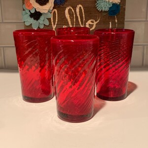 May include: Set of three red glass tumblers with a swirl design. The glasses are clear and have a textured surface.